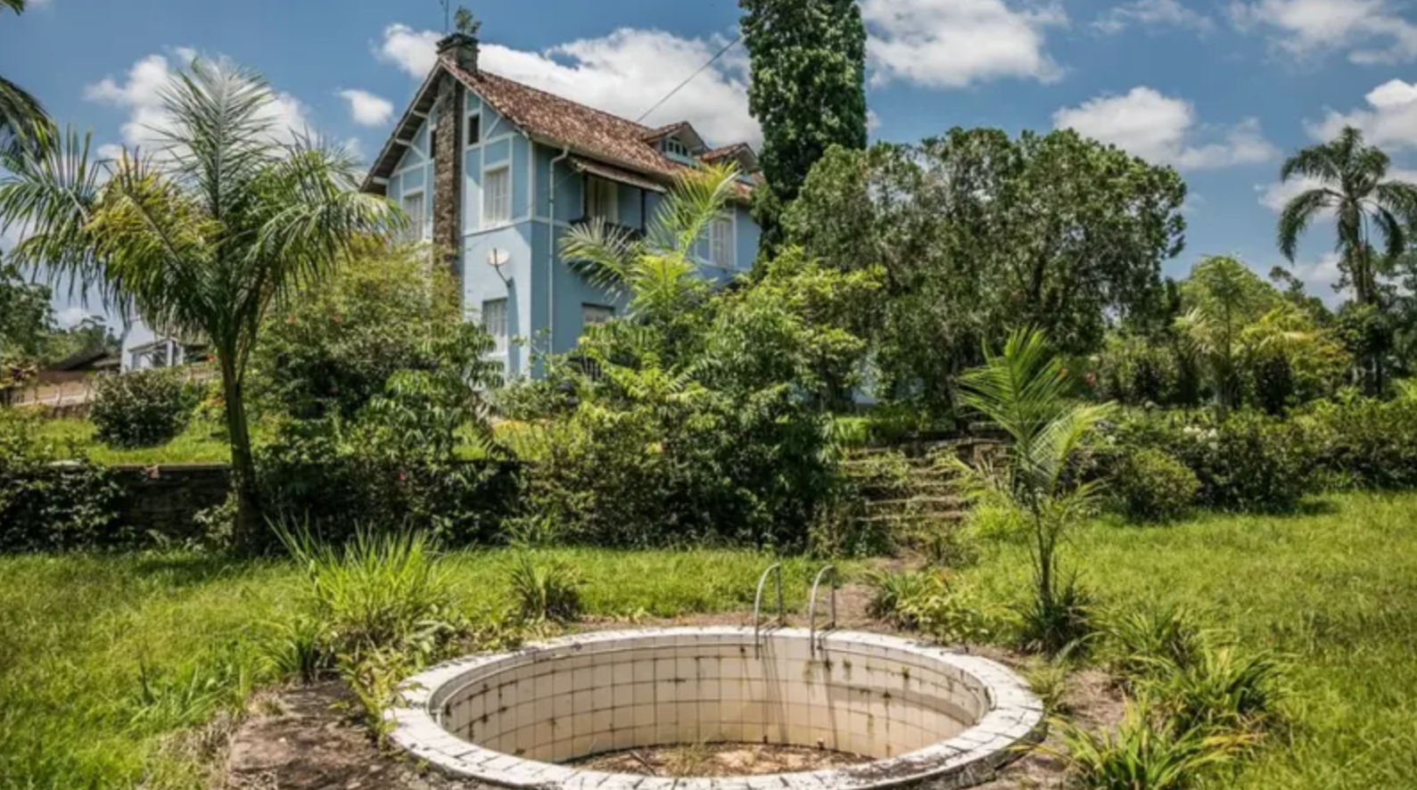 Piscina vazia, com casarão ao fundo em paisagem rural