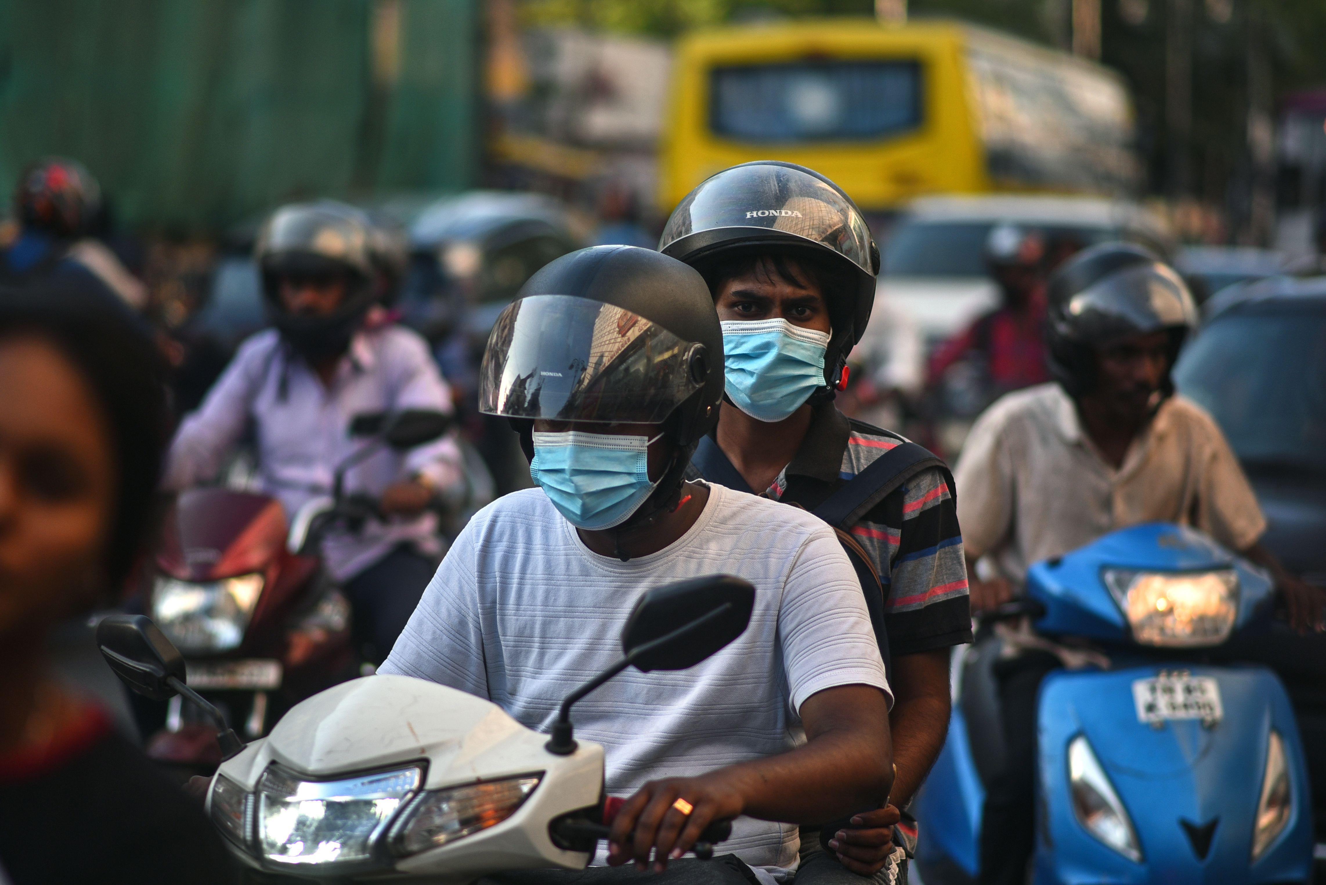 Dois homens em uma scooter usam máscaras faciais