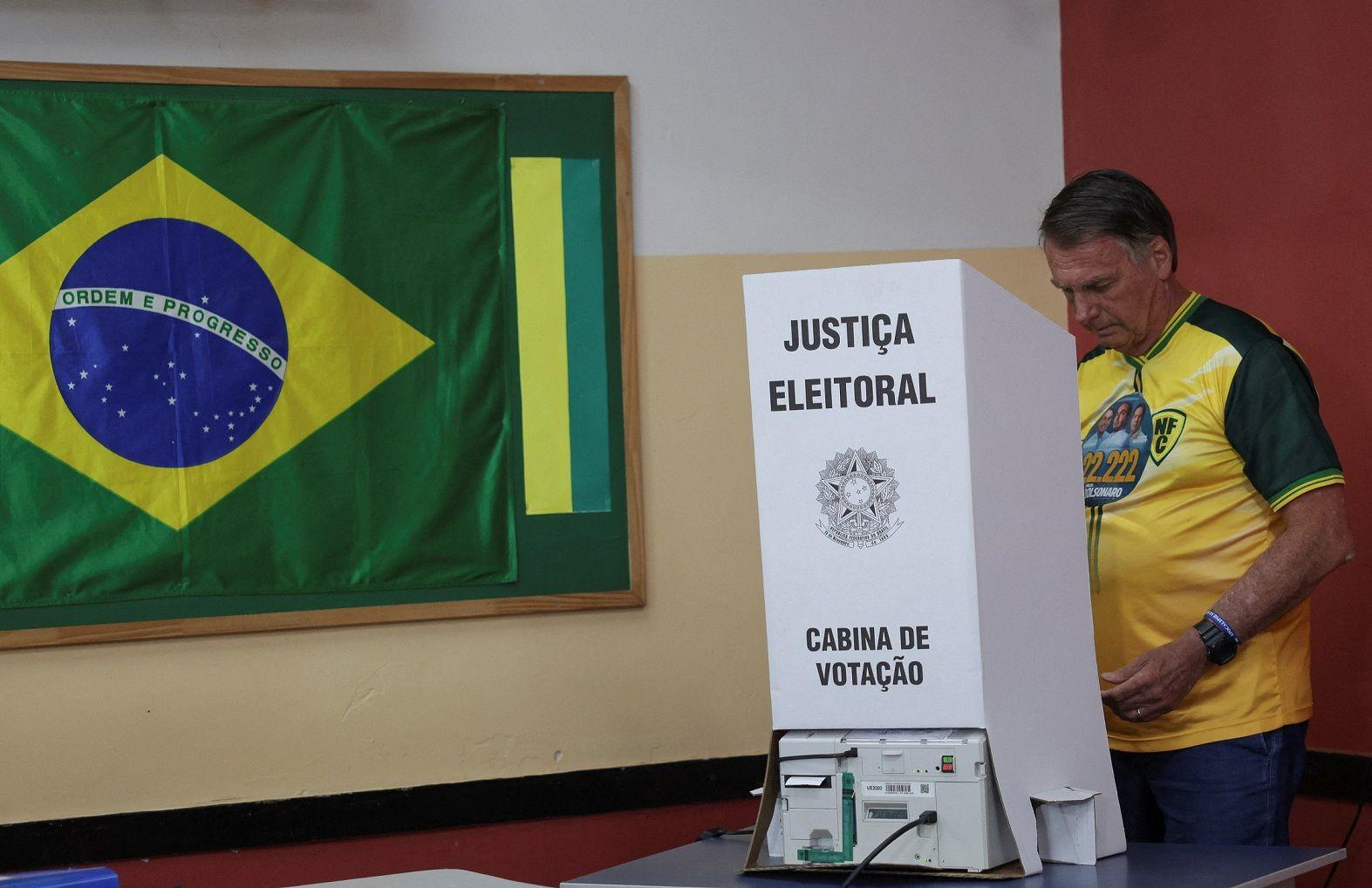 Jair Bolsonaro atrás da urna de votação, com bandeira do Brasil ao lado