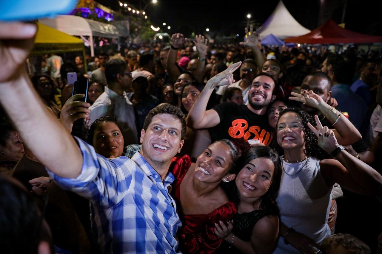 João Campos segurando um celular e tirando foto com a população na rua 