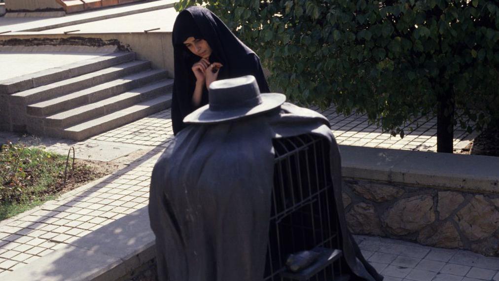 A young woman, fully covered in Islamic chador, viewing Rene Magritte's sculpture 'The Healer' in the grounds of Tehran Museum of Contemporary Art