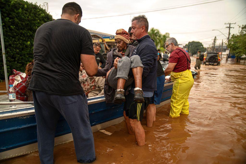 Mulher sendo carregada no colo e colocada dentro de barco de resgate em meio à enchente