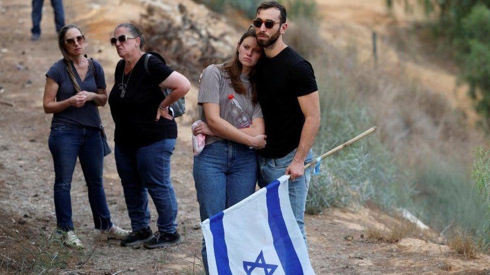 Um homem segura uma bandeira israelense durante o funeral de um casal que foi morto na infiltração mortal de Israel por homens armados do Hamas na Faixa de Gaza, no Kibutz Ruhama, no sul de Israel