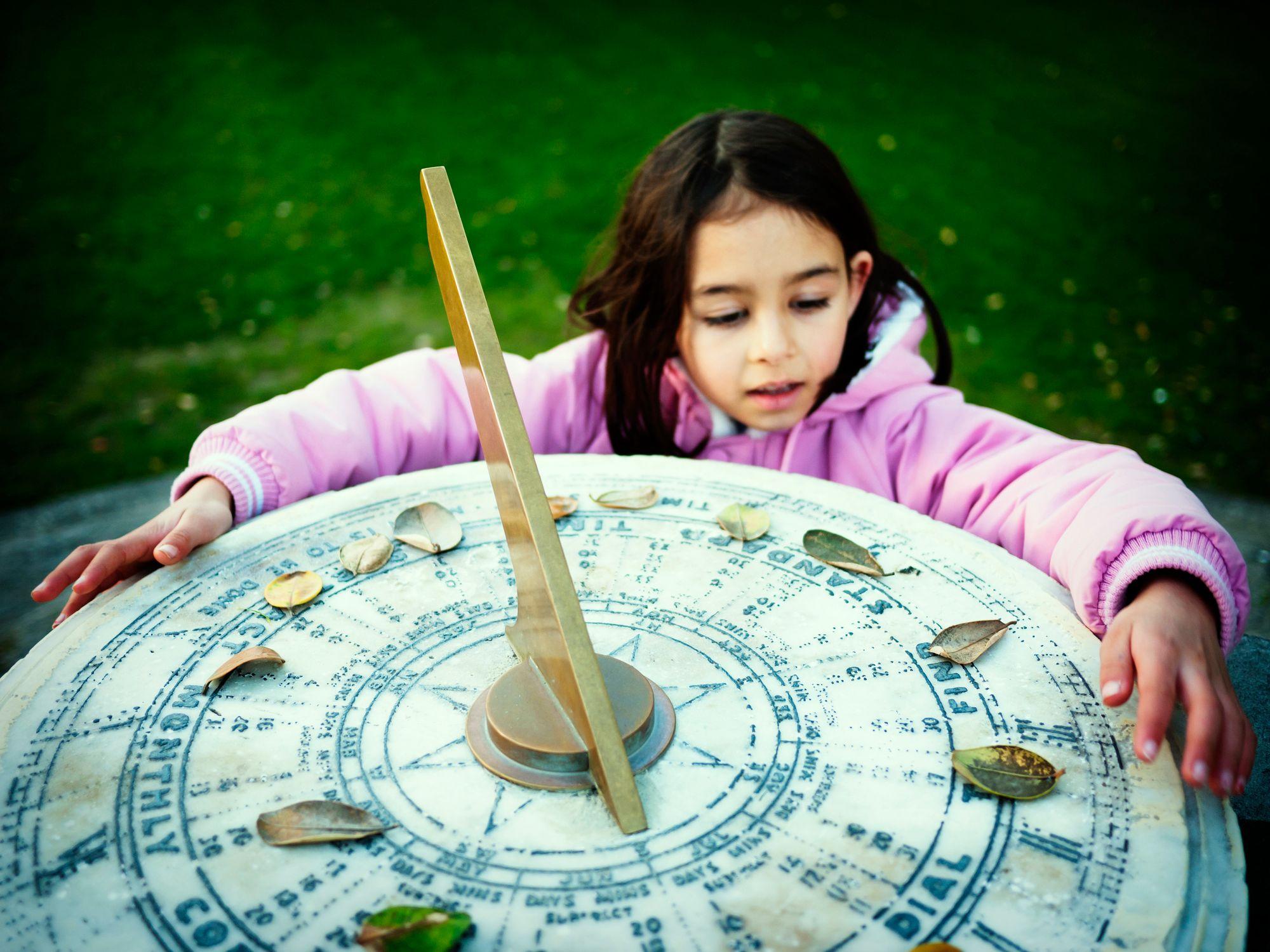 Niña al lado de un reloj de sol