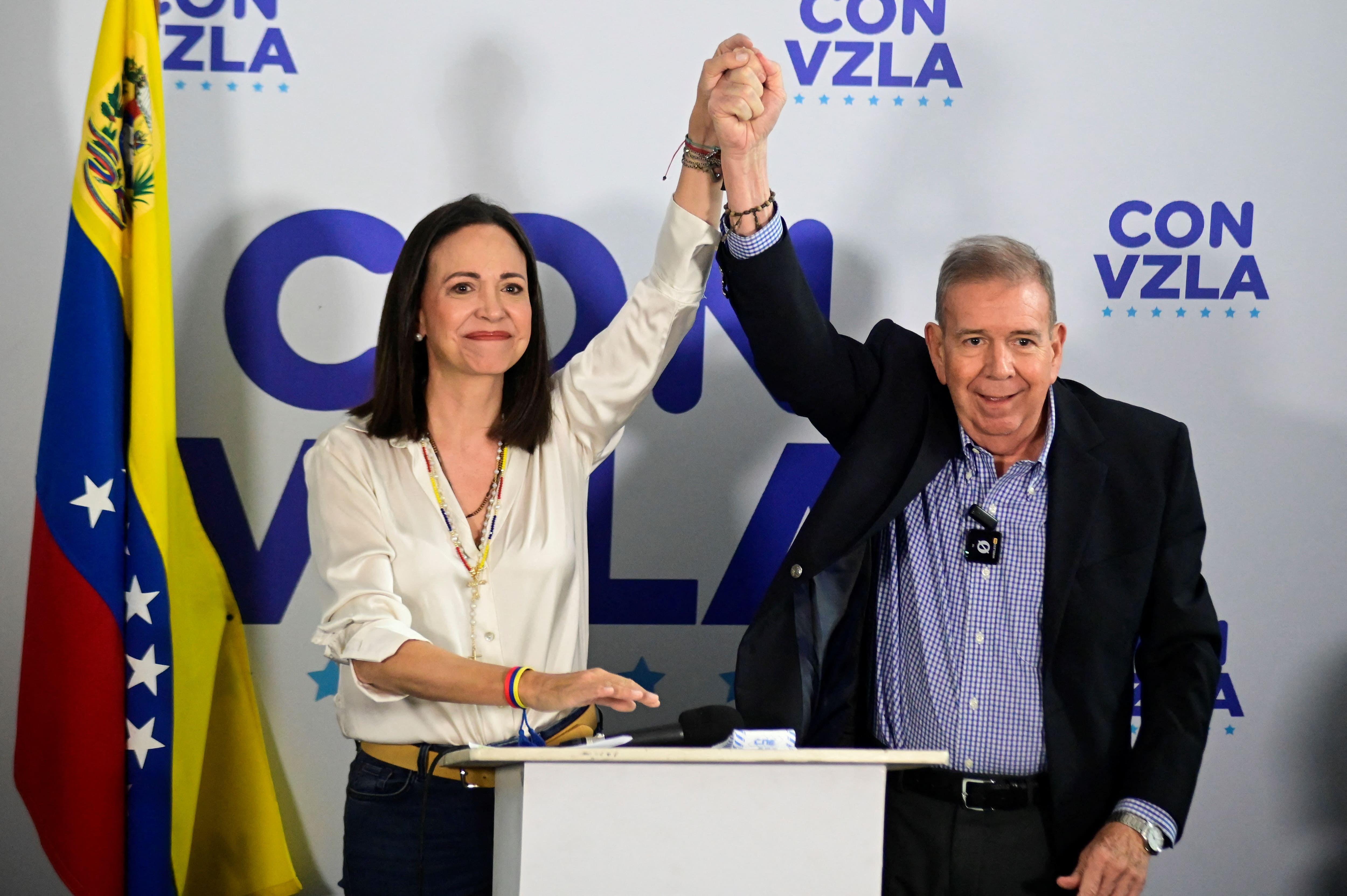 Maria Corina Machado e Edmundo González de mãos dadas, sorridentes. 