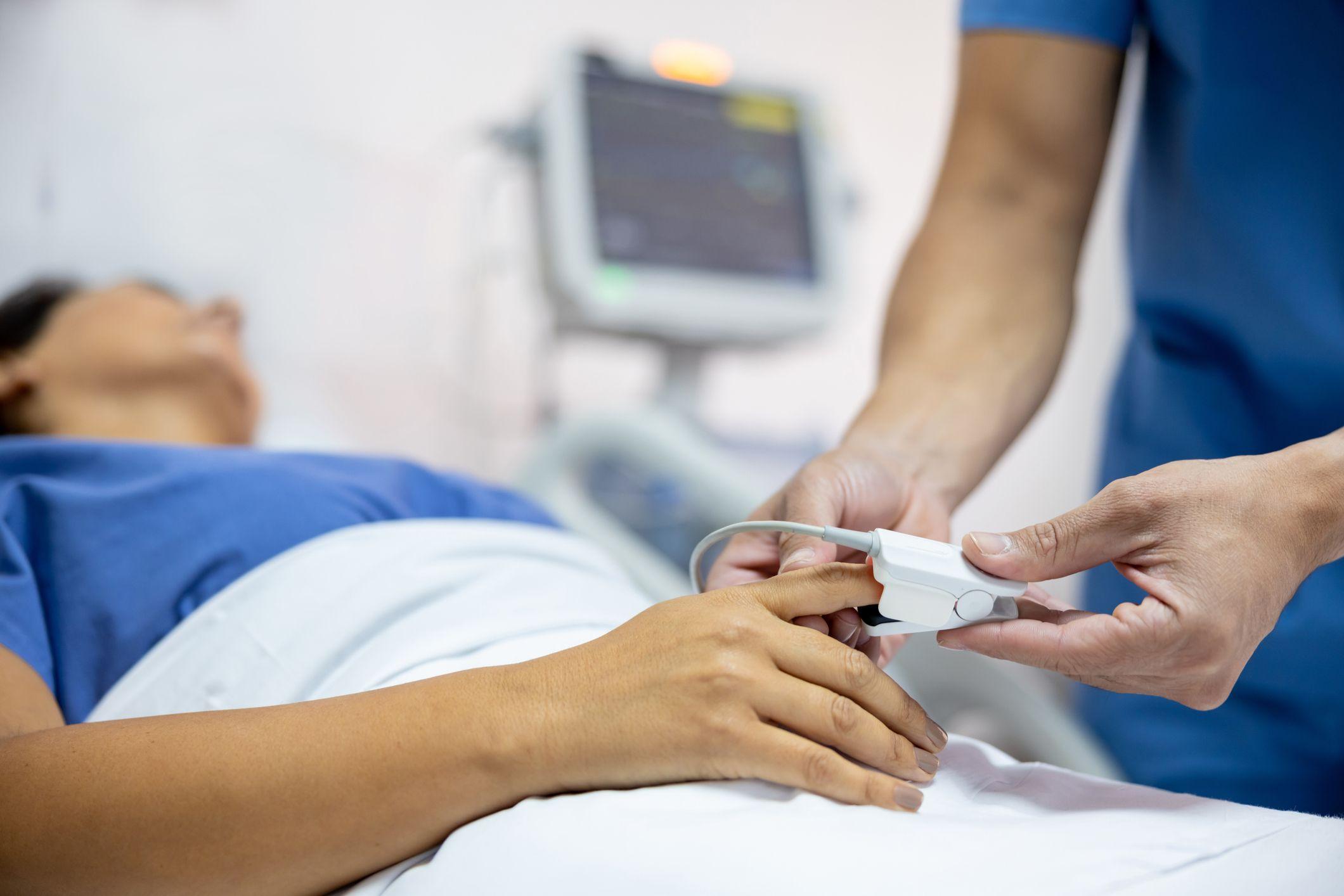 Profissional de saúde colocando oxímetro em mulher deitada no hospital