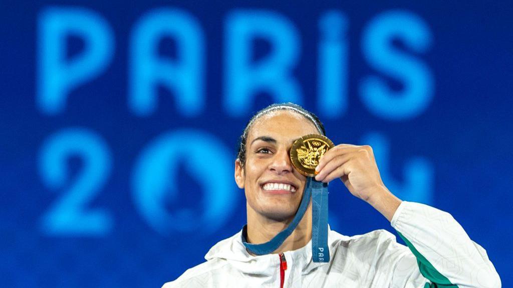 Imane Khelif posa segurando sua medalha de ouro sobre o olho