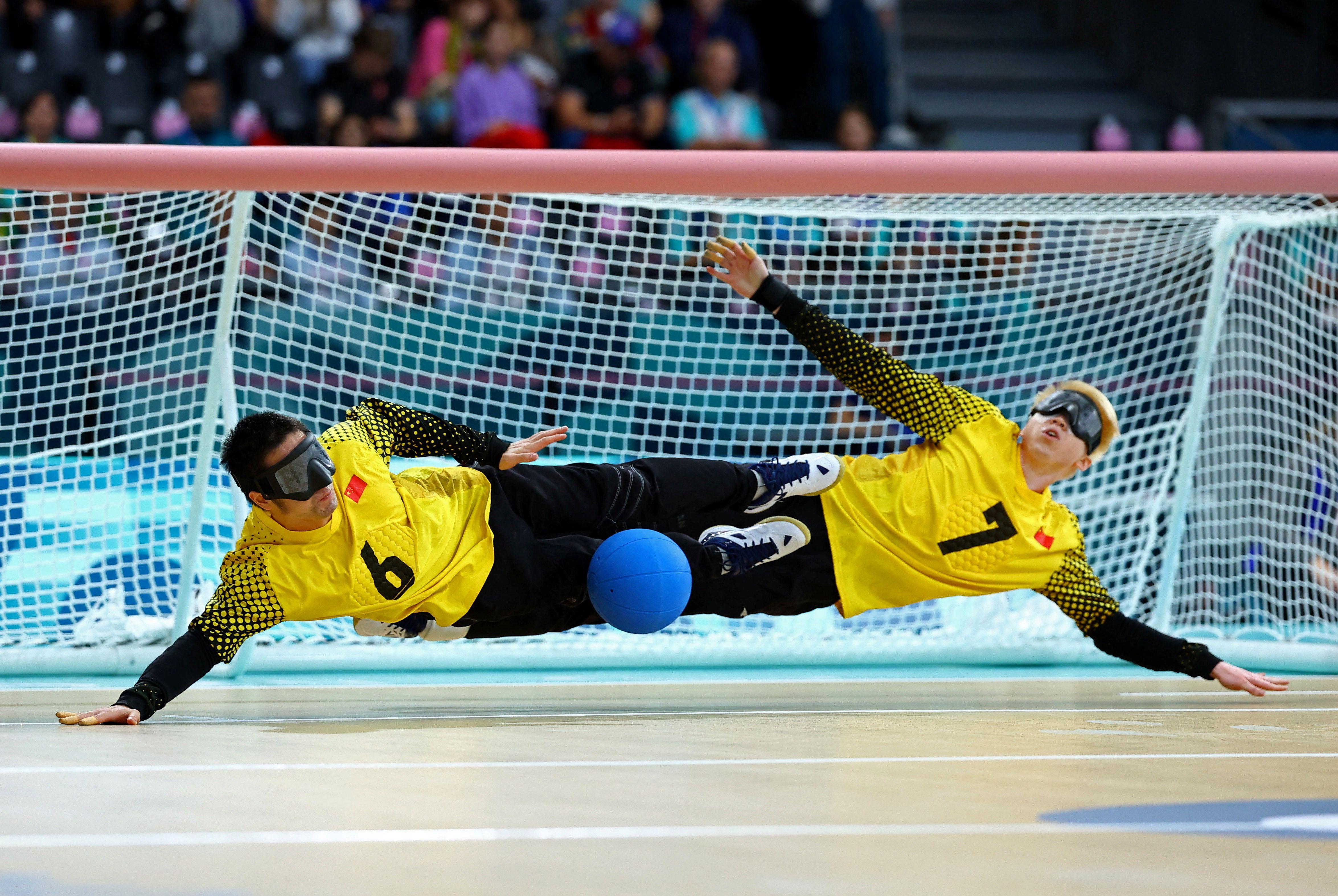 Dos personas con gafas oscuras  intentan detener una pelota azul 