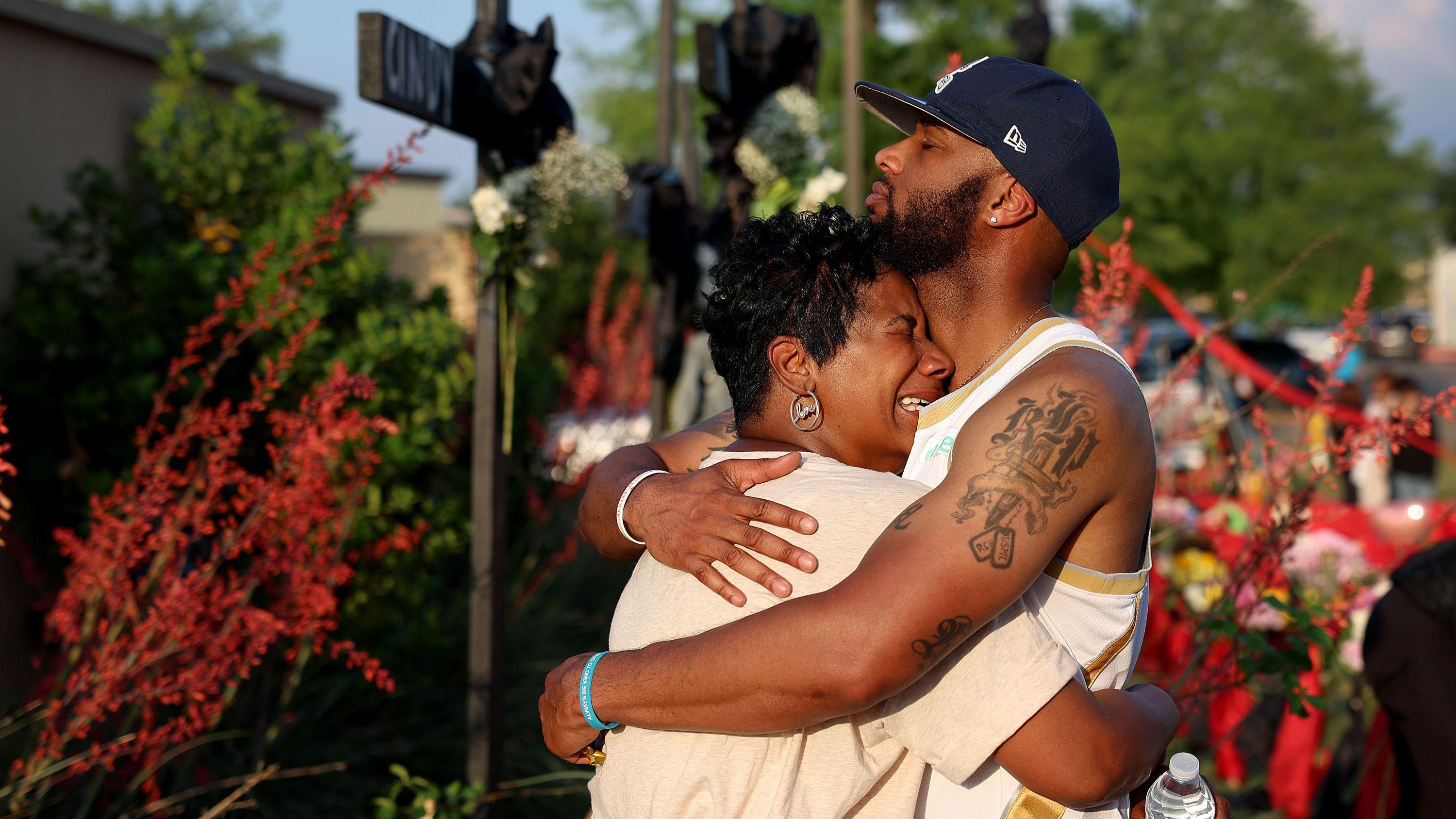 Hijo consuela a su madre frente a un memorial cerca de la escena del tiroteo de Allen Premium Outlets 