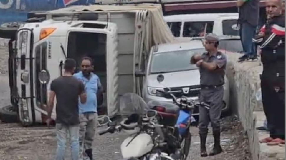 مواطنون وعنصر من الدرك اللبناني يقفون بجوار الشاحنة المقلوبة