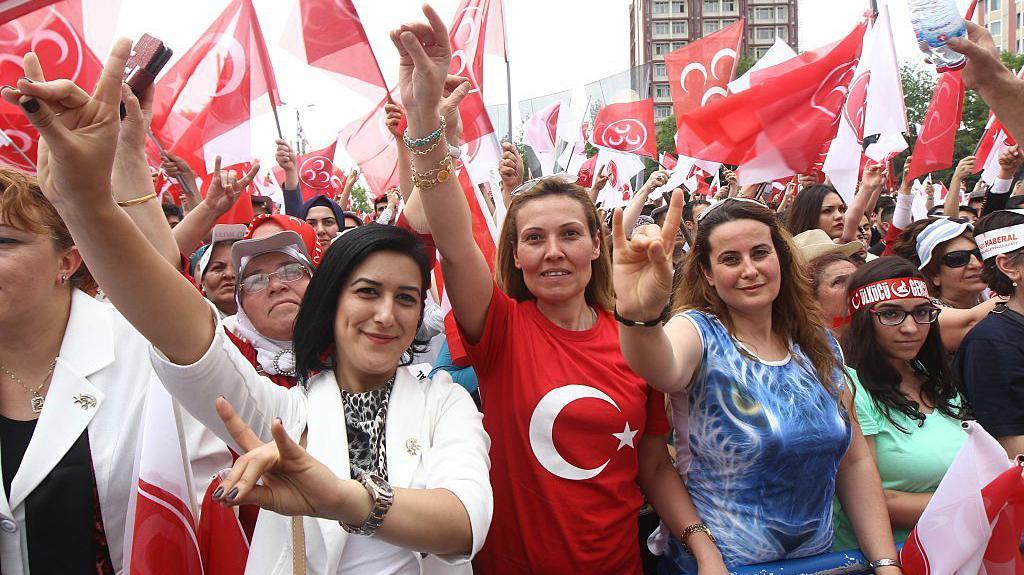 Women during a nationalist event make the wolf salute 