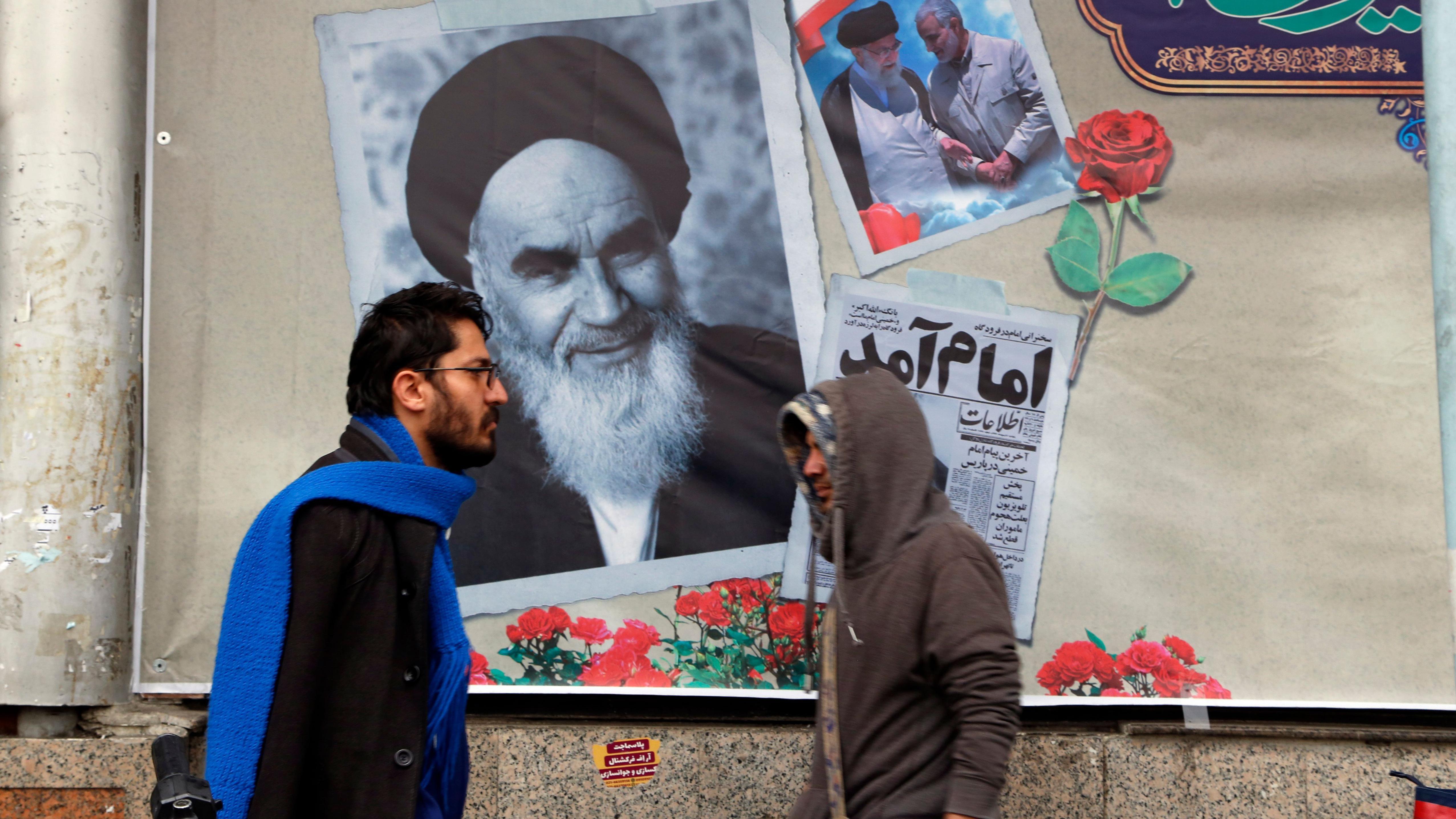 Dos hombres ante una pared donde hay una imagen del ayatolá Jomeini