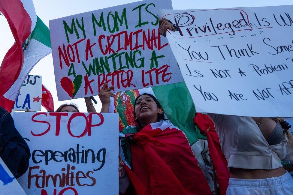 Una joven con una bandera de México y una pancarta en inglés que dice: "Mi mamá no es una criminal por querer una vida mejor"