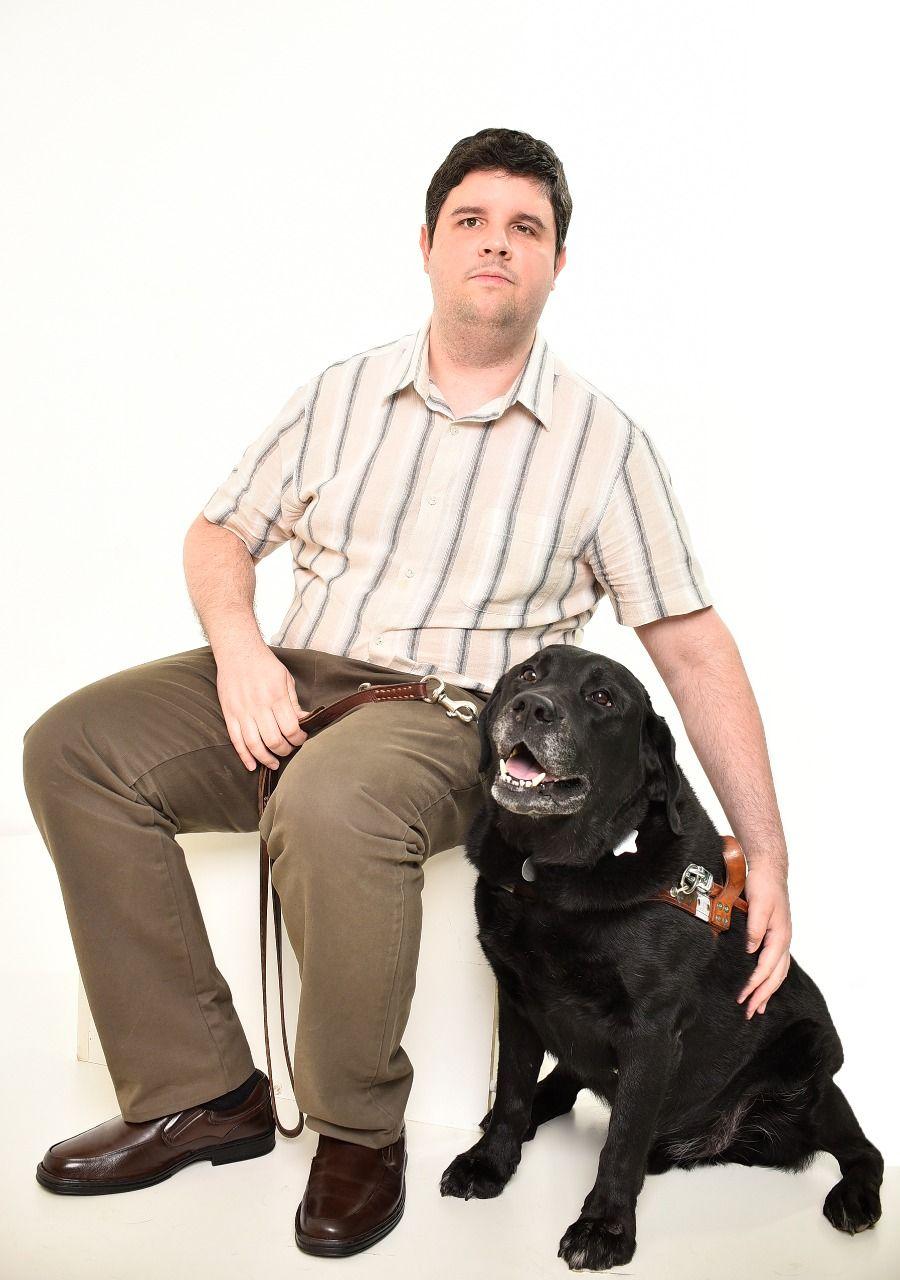 Spencer sentado e usando camisa de manga curta ao lado de seu cão-guia Wade, um labrador