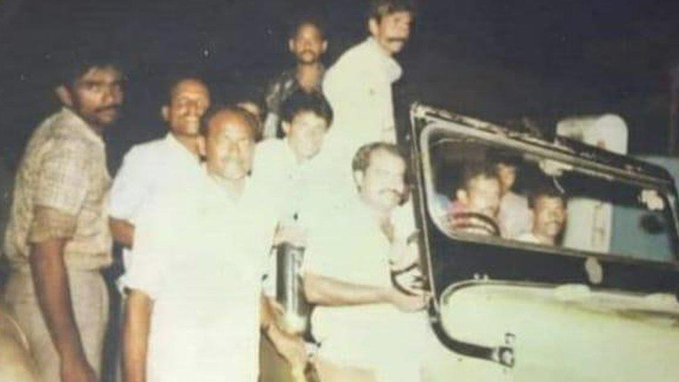 Vários homens dentro e ao lado de um carro, em foto antiga
