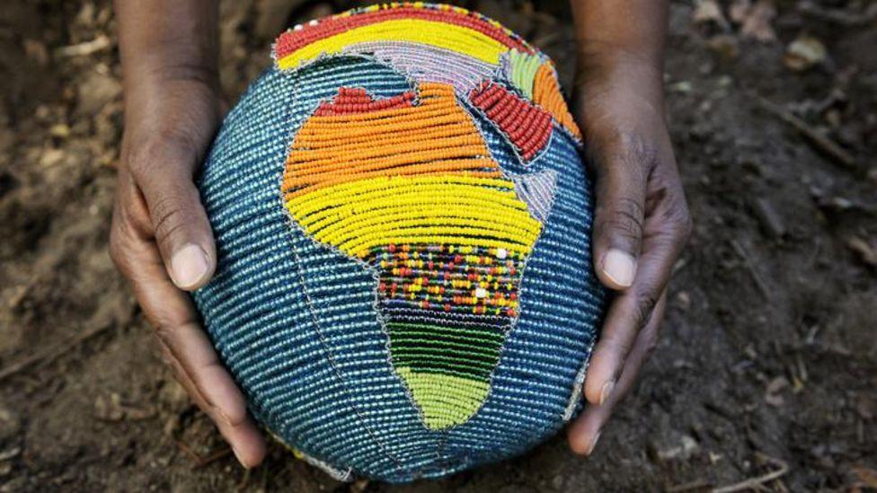 Las manos de una mujer sostienen un globo terráqueo hecho de cuentas que muestra el contiente de África