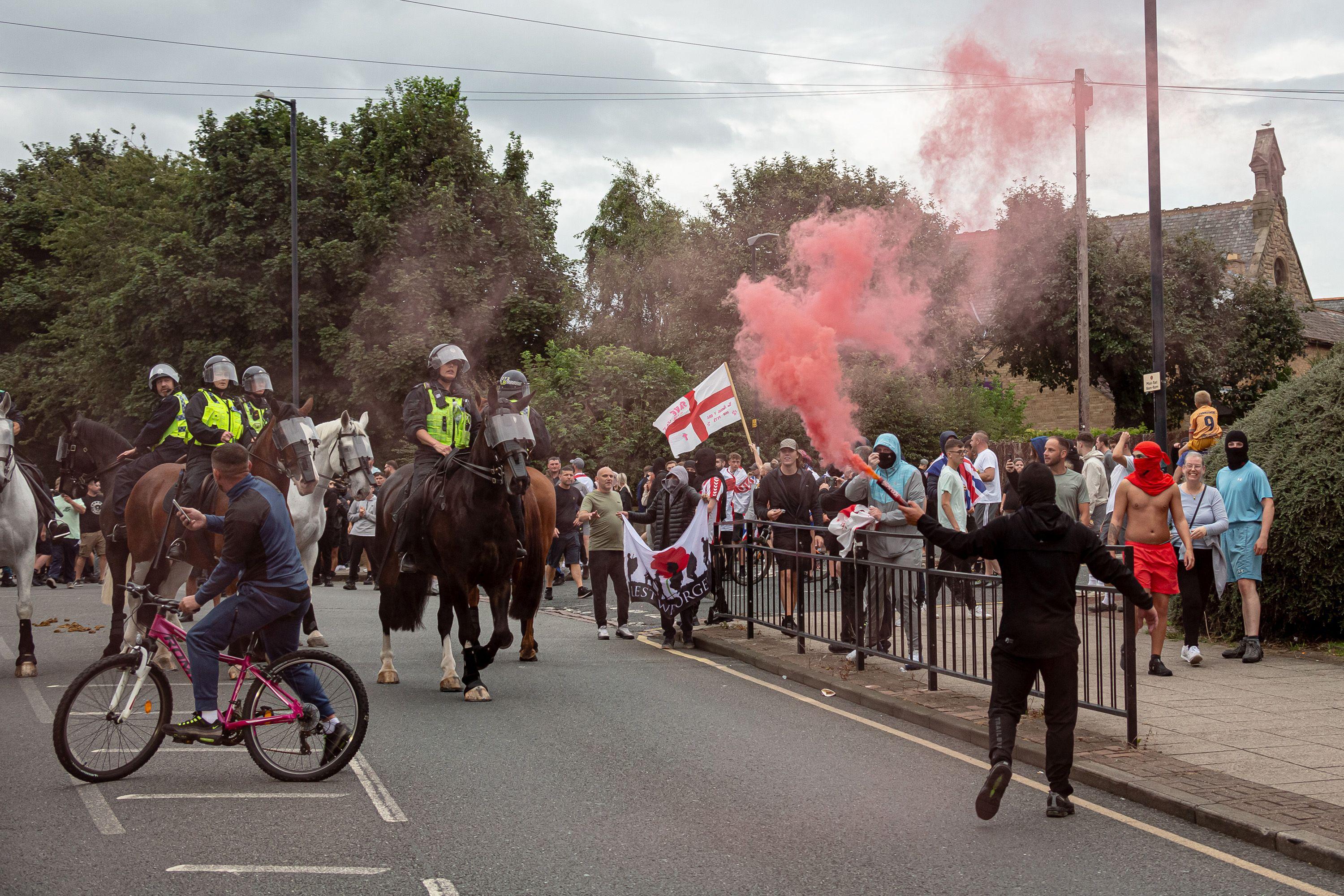 A hooded individual sets off a red smoke flare next to police on horses in Sunderland