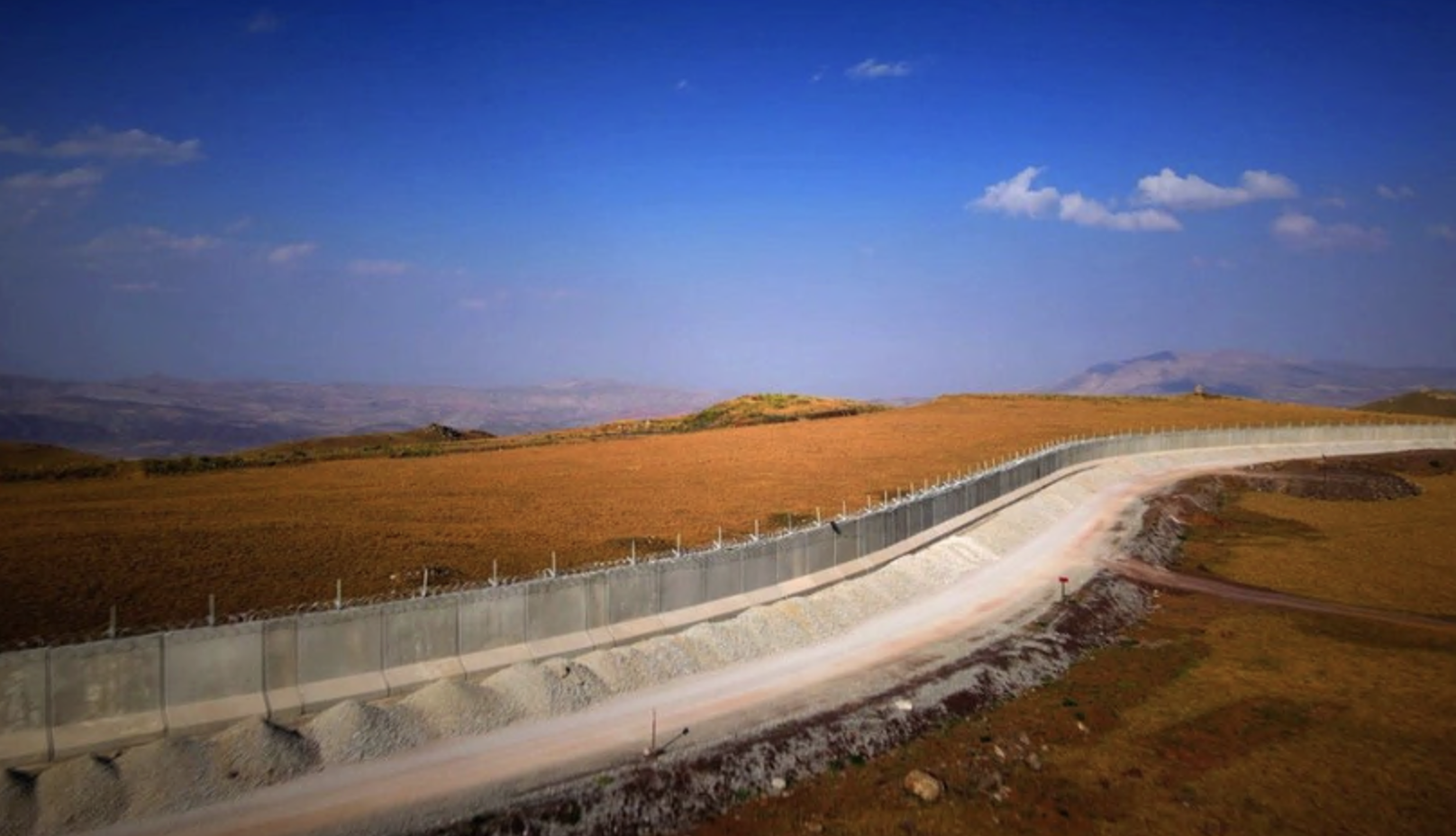 Concrete border wall runs along landscape with blue sky above