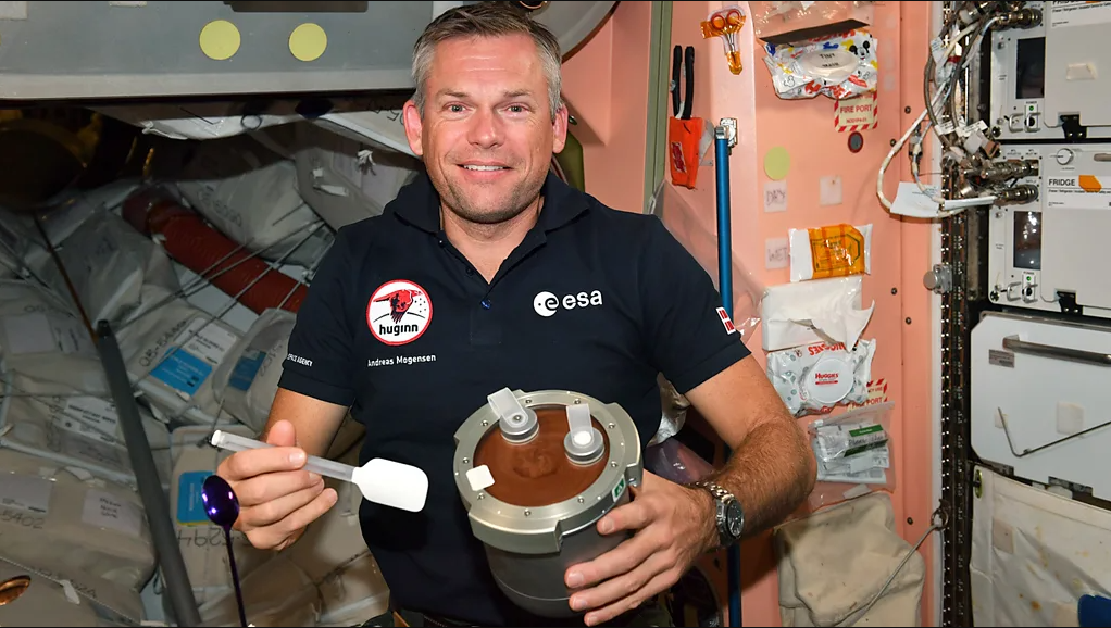 Astronauta Andreas Mogensen dentro de nave com pote cheio de apetrechos com mousse