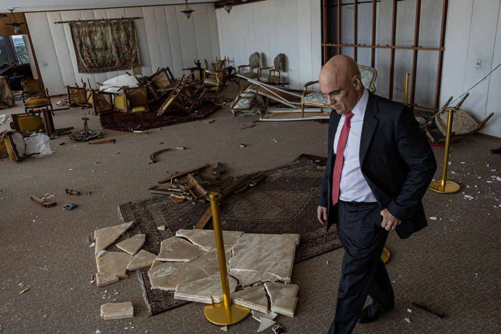 Alexandre de Moraes andando e olhando para baixo em uma sala destruída