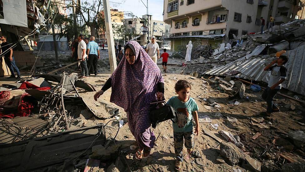 Mujer caminando con una niña de la mano entre escombros tras los bombardeos