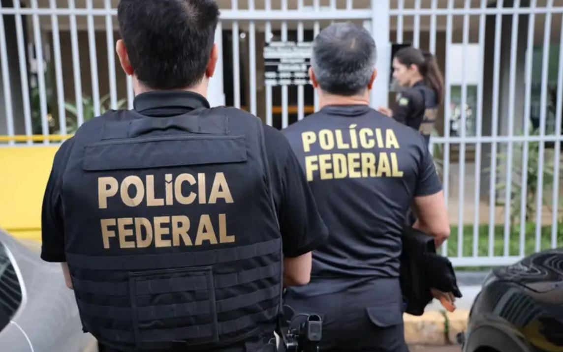 Imagem de dois agentes da polícia federal de colete, de costas, durante uma operação 