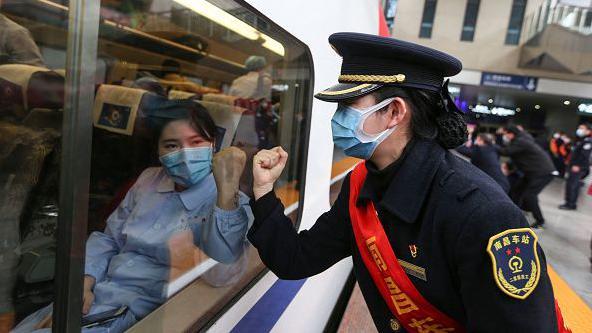 Nesta foto, de fevereiro de 2020, uma funcionária do sistema ferroviário chinês (à direita) saúda uma profissional de saúde que se dirigia a Wuhan, o primeiro epicentro da crise sanitária