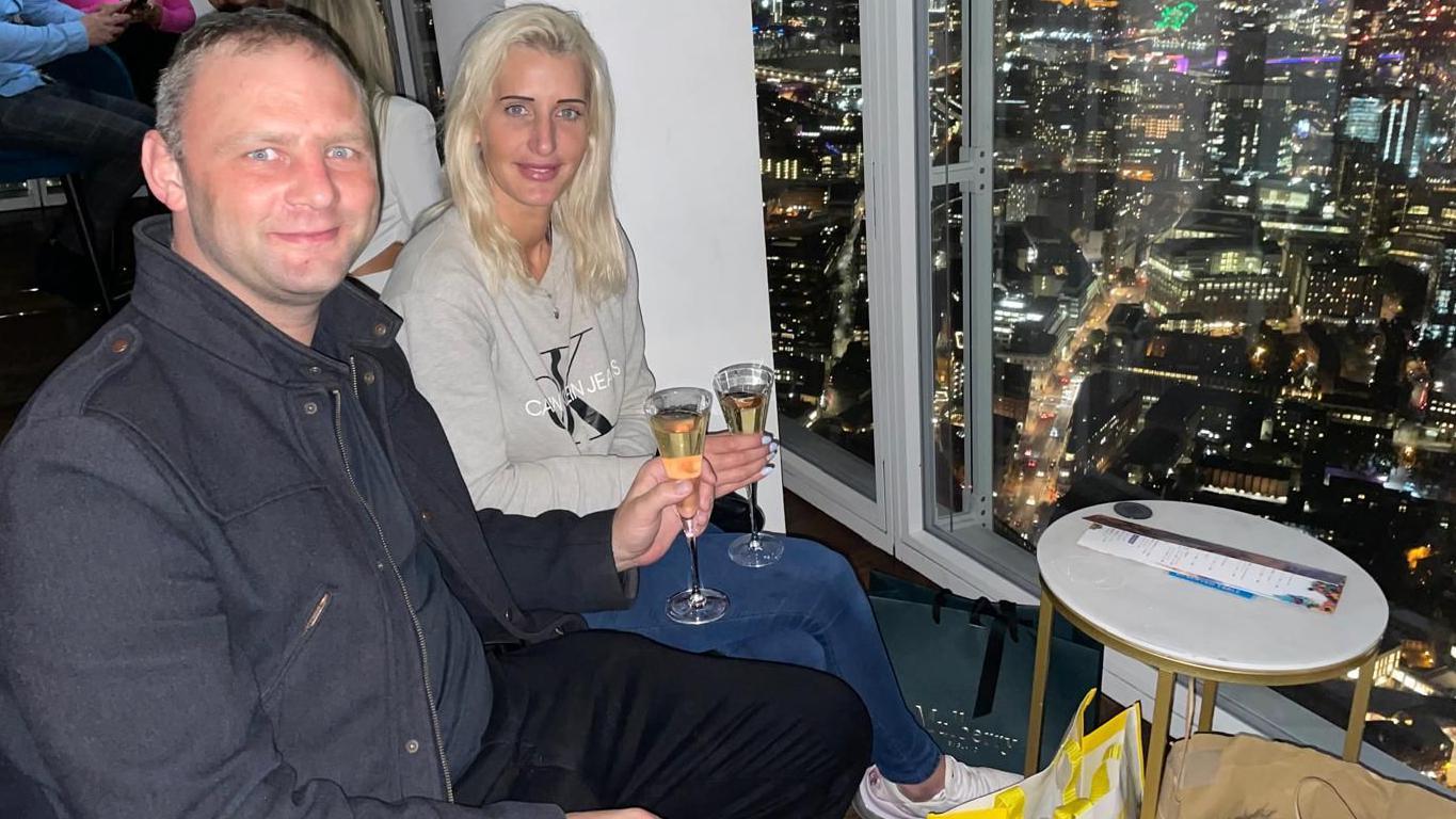 O casal sentado em um bar com uma taça de champanhe, com vista para Londres à noite