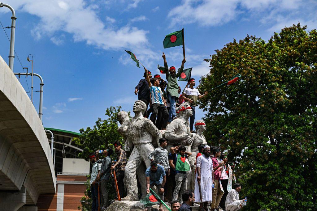Unos jóvenes sobre una estatua ondeando banderas de Bangladesh