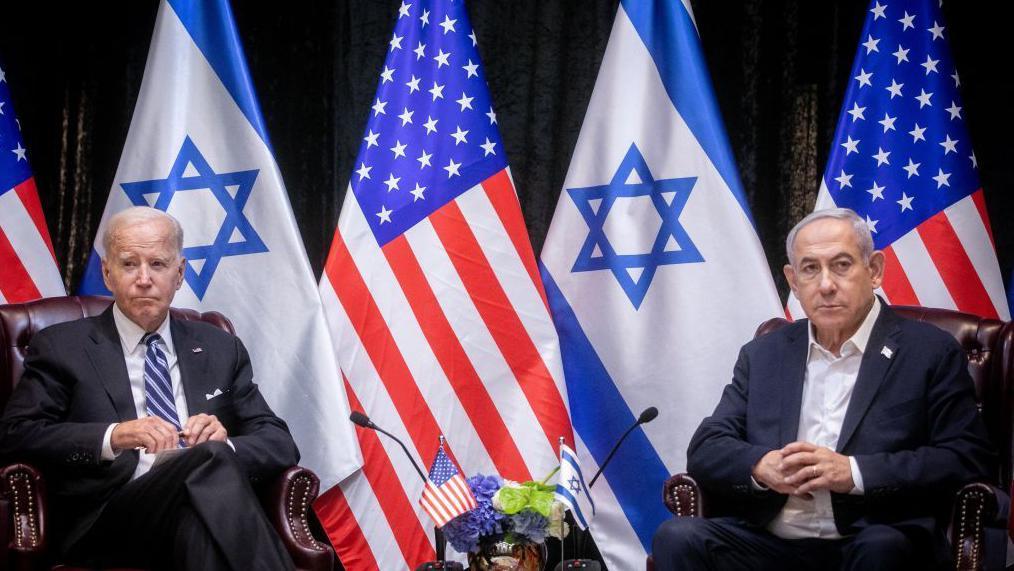 Joe Biden y Benjamín Netanyahu, sentados en sillones distintos con las banderas de sus países de fondo. 