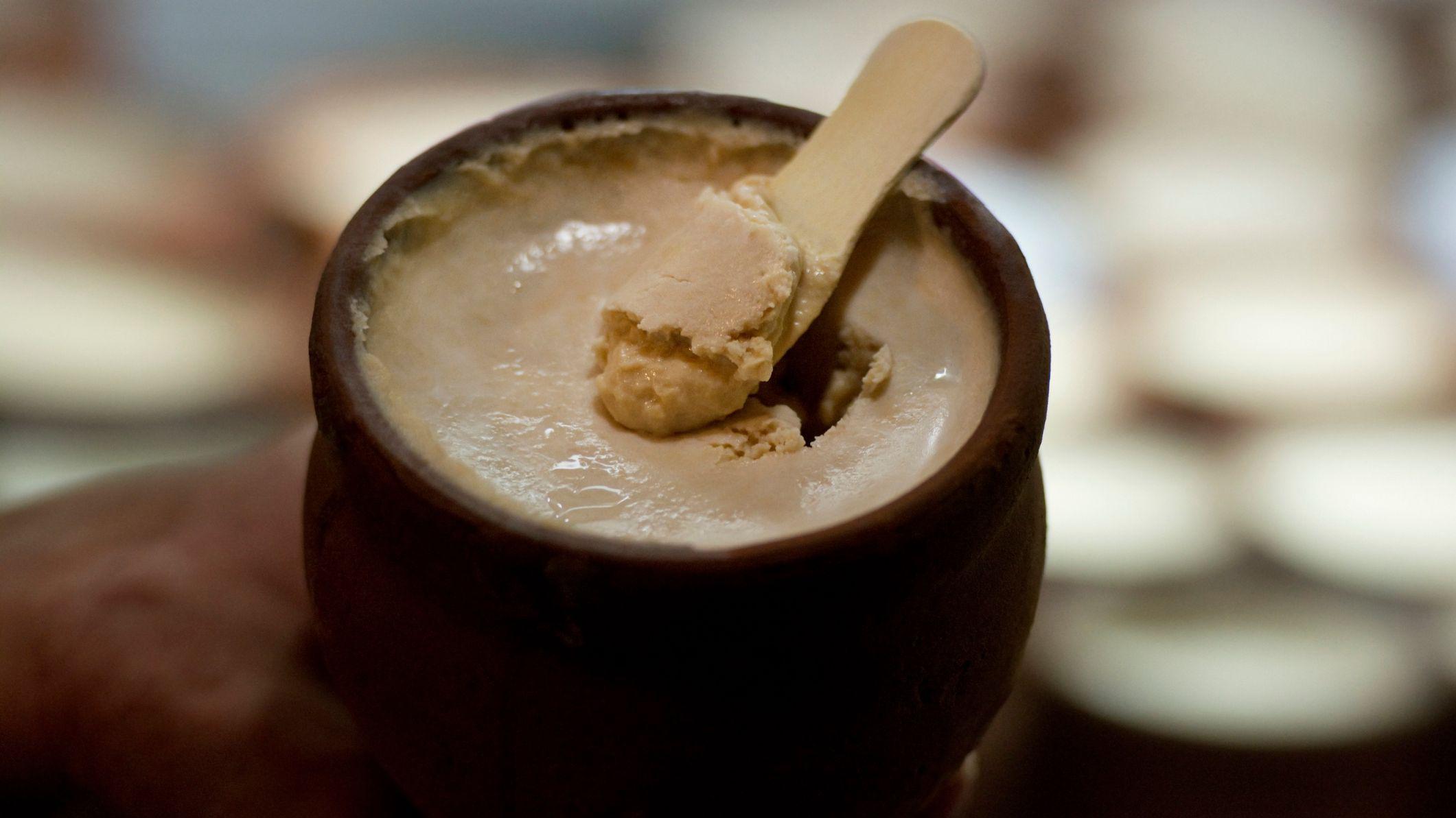 Uma pequena pazinha de madeira mergulhada em uma panela de barro com kulfi, sobremesa gelada indiana