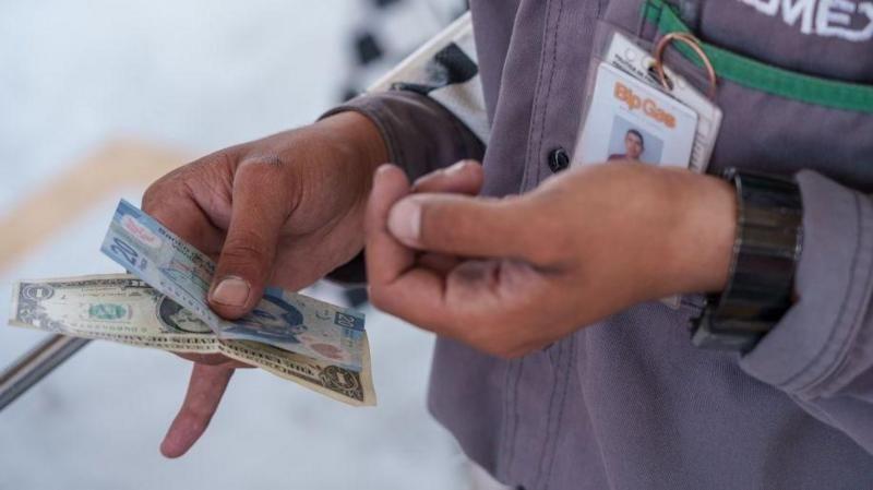 Pessoa com colete e crachá examina notas de duas moedas diferentes