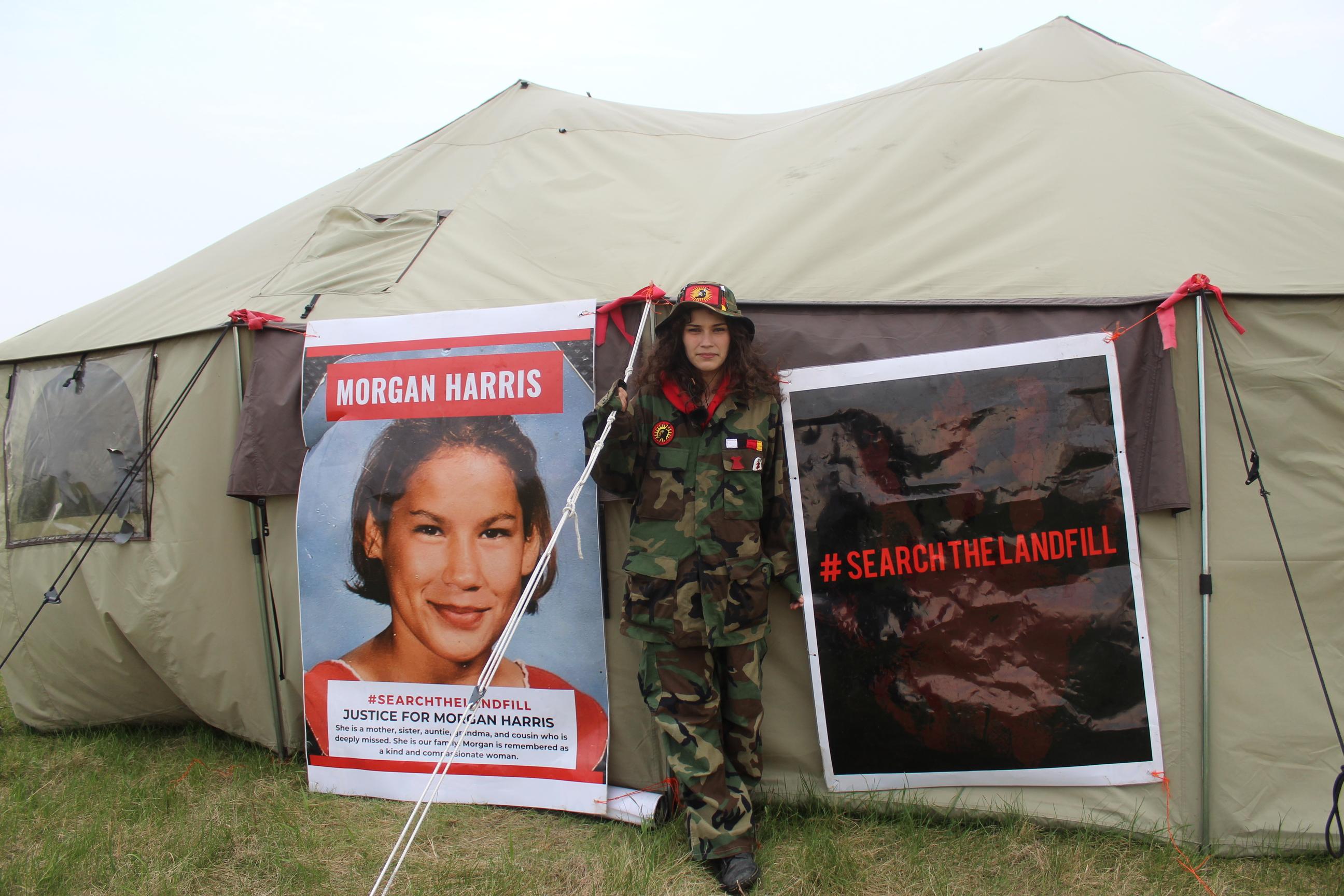 Cambria Harris in front of a tent with signs calling for the search for the body of her mother, Morgan Harris.