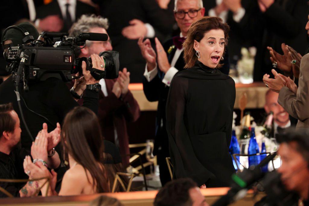 Fernanda Torres em pé, boquiaberta, entre pessoas assistindo o Globo de Ouro