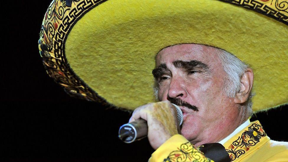 Vicente Fernández vestido de amarillo con un micrófono