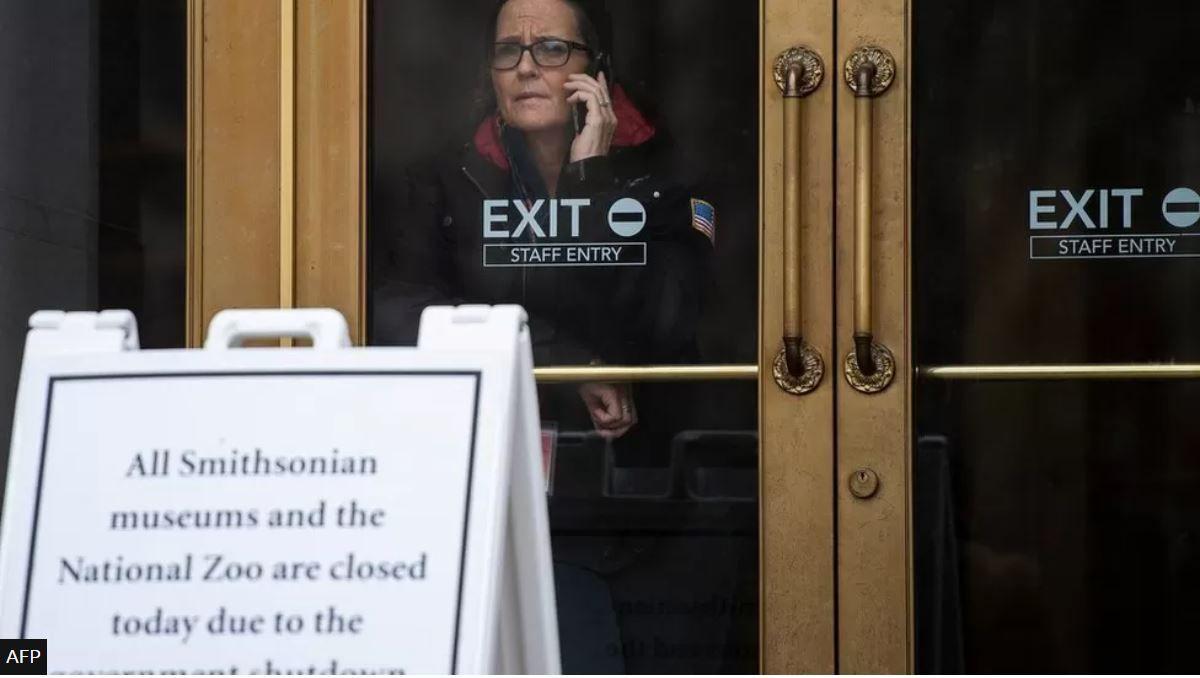 موظفة حكومية أمريكية تتحدث عبر الهاتف وتنظر من الباب الزجاجي لمتحف مغلق في واشنطن خلال إغلاق 2019