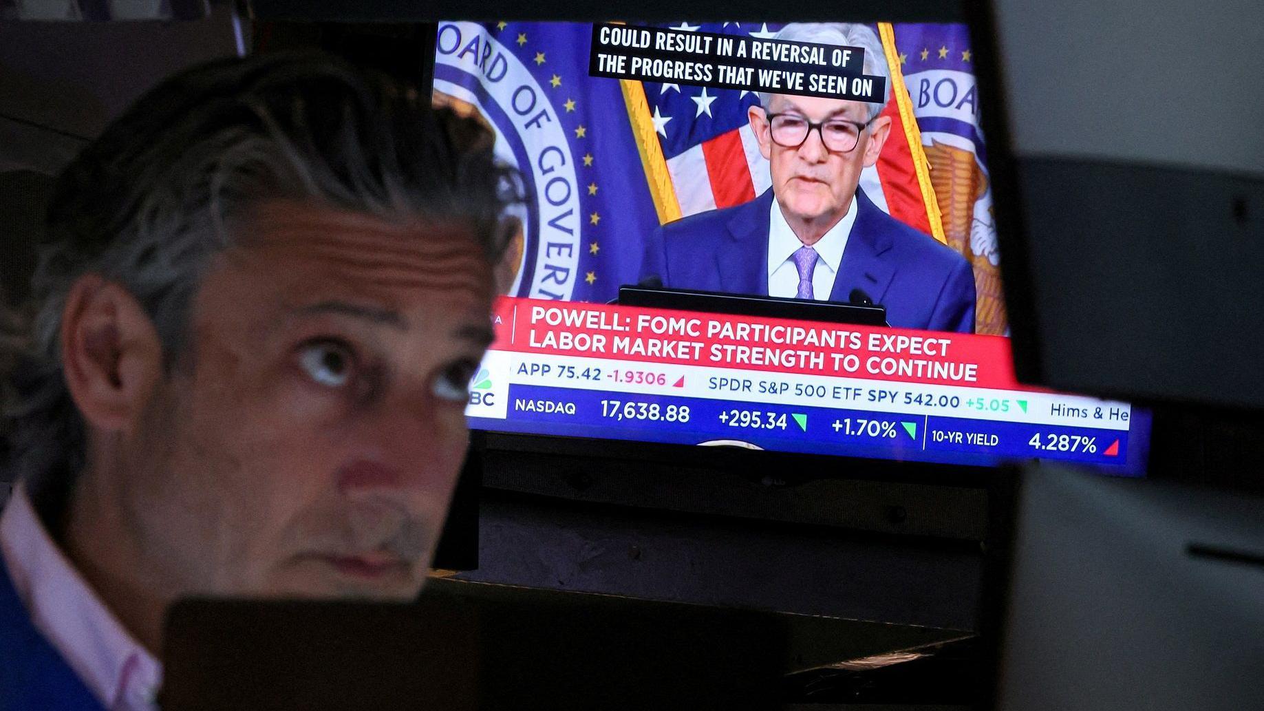 Um operador de ações da Bolsa de Nova York trabalha enquanto observa numa televisão o presidente do Fed, Jerome Powell, discursando