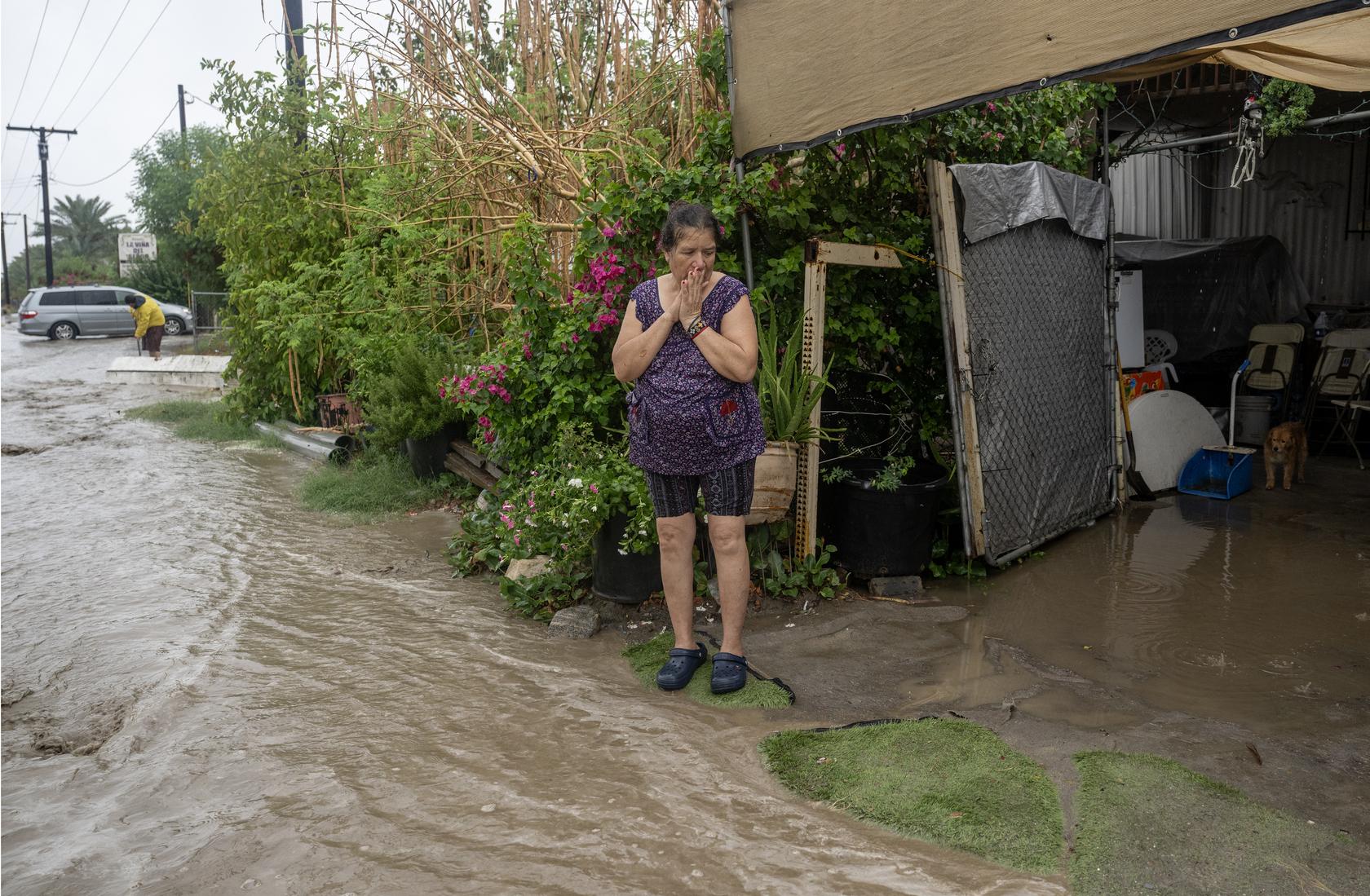 María Elena Zaragoza observa cómo las fuertes lluvias empujan las aguas de la inundación hacia su entrada mientras la tormenta tropical Hilary arroja lluvias torrenciales en Thermal, California.