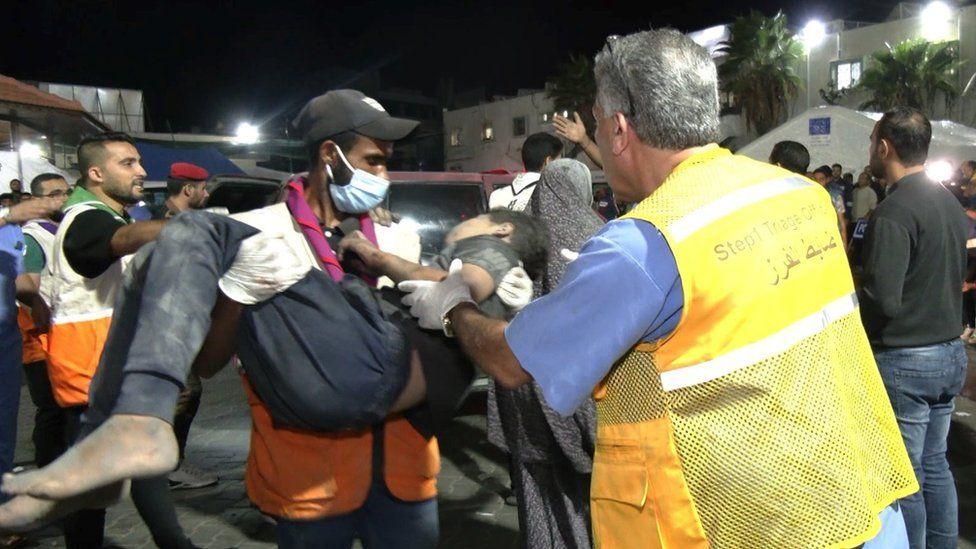 A paramedic carries a child in his arms from an ambulance to the hospital