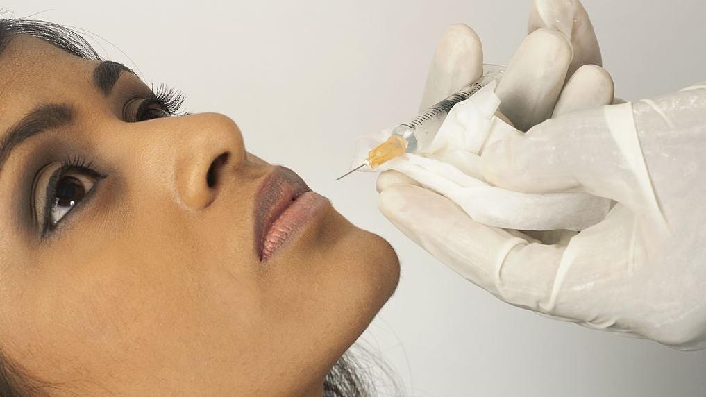 Doctor injecting collagen into young woman's lip