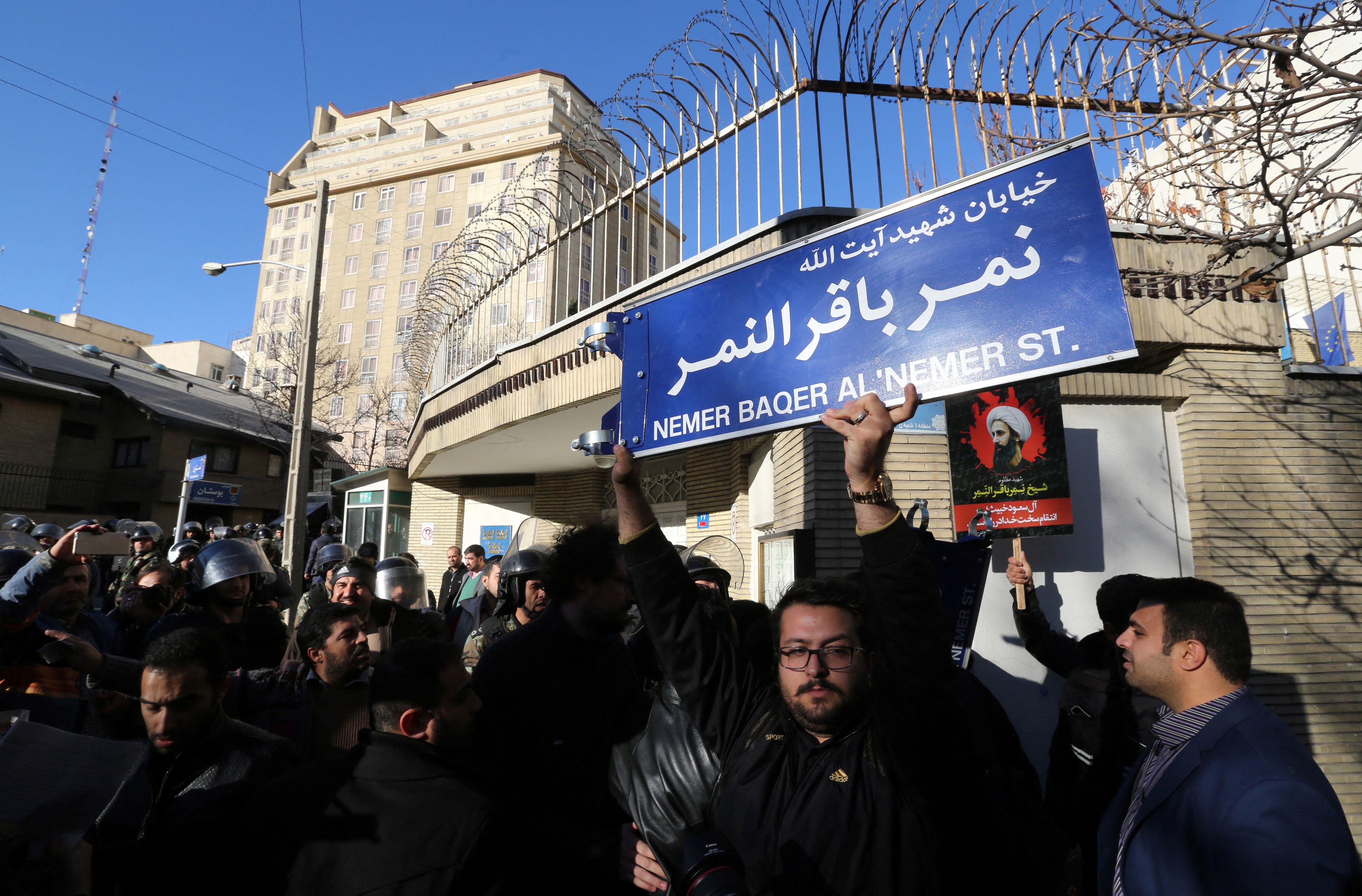 متظاهر إيراني يحمل لافتة شارع تحمل اسم رجل الدين الشيعي البارز نمر النمر خلال مظاهرة احتجاجاً على إعدامه من قبل السلطات السعودية، أمام السفارة السعودية في طهران، بتاريخ 3 يناير/كانون الثاني 2016.