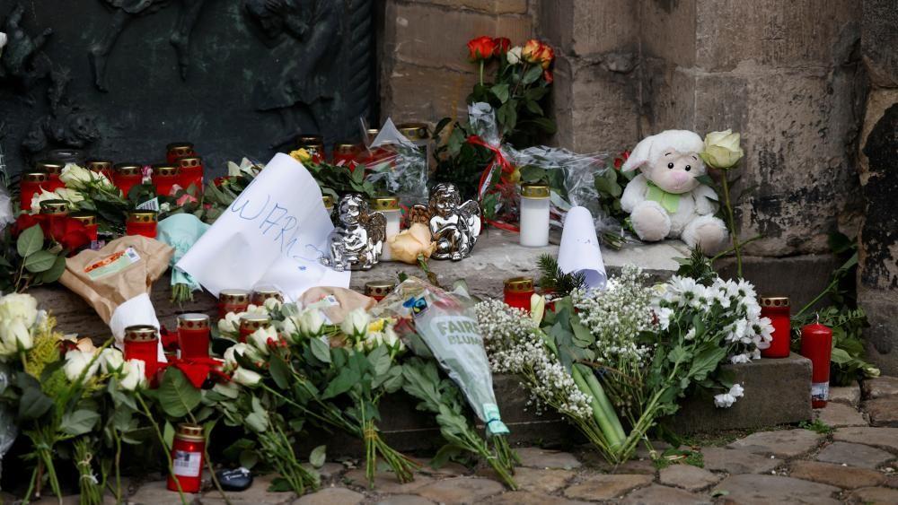 Buquês de flores, velas e ursinhos de pelúcia encostados nos degraus de um memorial improvisado