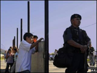 Crianças observam policial que guarda obras de muro na Argentina (AP, 8/4)