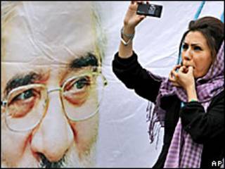Una mujer se toma una foto junto a un cartel de Hossein Mousavi