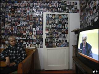 Una mujer bosnia de Srebrenica mira en TV el juicio de Karadzic. De fondo una pared cubierta con víctimas de la masacre de Srebrenica