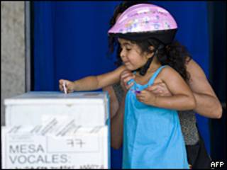 Una niña introduce el voto de su madre en una urna, en Chile