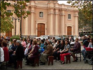 Personas sentadas en la calle oyen la misa