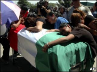 Mujeres lloran ante un ataúd con la bandera mexicana