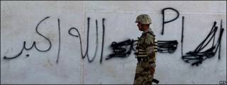 Un soldado iraquí camina frente a una pared con el grafitti: "Dios es grande"
