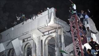 卡扎菲支持者在的黎波里被炸毀的建築物上喊口號(25/4/2011)